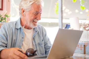 Smart work concept. Smiling senior man in coffee shop while working on laptop talking on phone. Elderly man people enjoying free lifestyle doing job from remote