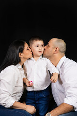Father and mother kissing their son on the cheek on a black background.