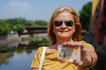 proud and smiling old immigrant woman showing her ID (Spanish national identity document) outside....