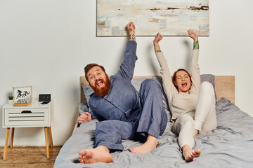 excited people, day off without kids, redhead and happy husband and wife, bearded man and woman with raised hands, parents alone at home, modern lifestyle