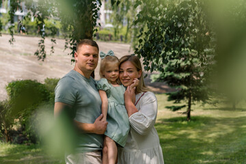 Fototapeta premium Portrait of a smiling young family mom dad and little daughter family on a walk in the park happy childhood