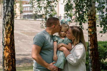 Fototapeta premium Portrait of a happy young family mom dad and daughter parents hold a baby girl in their arms and kiss her family on a walk in the park childhood