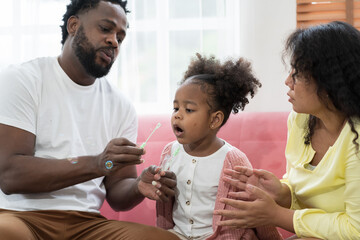 Happy mother and father playing blowing soap bubbles with their daughter.Happy African American little girl kid playing with dad. Happy African American family spending time together