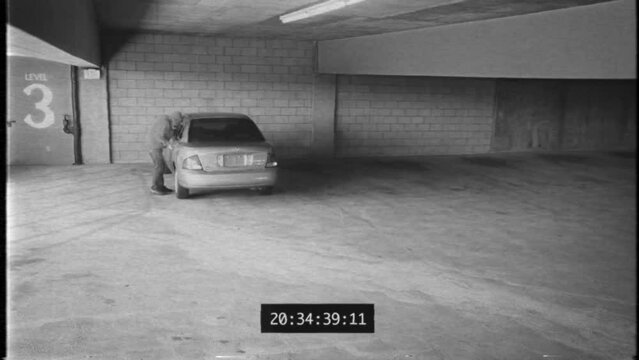 Security camera footage of a car in a parking deck being broken into.