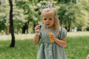 Fototapeta premium portrait Cute little girl blowing soap bubbles having fun in the park on a summer day Child playing Happy Children's Day Fun and carefree childhood