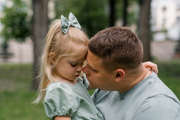 Happy family Young father holding baby in arms kissing her Father and daughter hugging each other outdoors in the park Father's Day