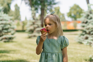 Fototapeta premium Little cute girl in green summer dress eating delicious ice cream Child with ice cream in city park summer family lifestyle Childhood
