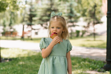 Fototapeta premium Little cute girl in green summer dress eating delicious ice cream Child with ice cream in city park summer family lifestyle Childhood