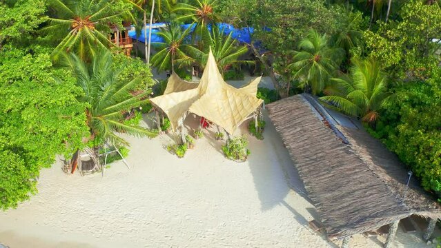 Aerial top view on white sand beach with sea and thatched huts and lush tropical island on Thinadhoo island in Maldives.