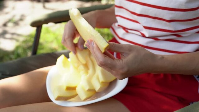 Closeup of hands young woman holding and breaks off piece of sweet melon over plate. Girl in a chair in the garden showing juicy pieces of cantaloupe. Fresh rockmelon for detox and body cleansing food