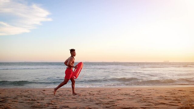 African American lifeguard running along the beach in Southern California at Sunset. Lifeguard's left hand is deformed.
