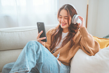 Happy asian woman listening to music from mobile phone while sitting on the the sofa at homes, Smiling girl relaxing with headphones in morning, Time to relax.