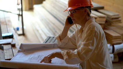 Profile shot of woman mechanical engineer on phone discussing and reviewing blueprints on a new...