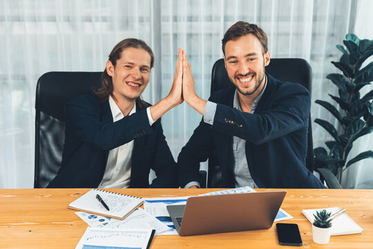 Businessmen celebrate success with joyous expressions, celebratory high-five hand gesture in office after analyzing data or achieving target. Teamwork and planning lead to successful outcome. Entity