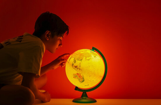 Portrait of a boy with the globe.  Closeup Young element school kid looking the map learning world geographic on lamp globe, dark room. 