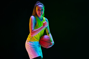 Winner. Young girl, basketball player in uniform posing with ball against black studio background...