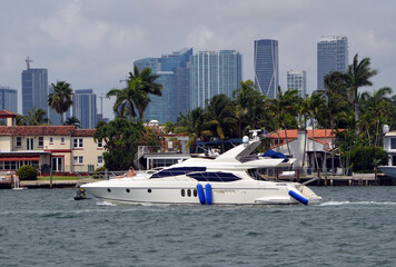 Obraz premium Party charter motor yacht leisurely cruising by luxury homes on Dilido Island,Miami Beach with downtown Miami tall building skyline in the background.