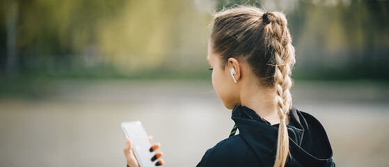 Young smiling girl making sport and running in the park using her phone to listen the music with...