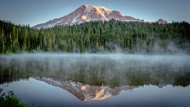 Mount Rainier and pine forest reflecting into Reflection Lakes at sunrise with light fog over lake | Mount Rainier National Park, Washington, USA
