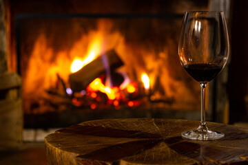 Glass of wine on a rustic wooden table in the background with a lit fireplace, moments of reflection