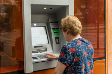 Senior woman is using a ATM. - obrazy, fototapety, plakaty