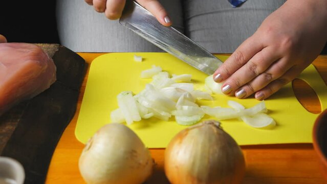 Women's hands cut onion for cholent with a large knife on a plastic board. close-up