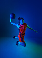 Slam dunk. Top view of young girl, basketball player throwing ball against blue studio background in neon light. Concept of professional sport, action and motion, game, competition, hobby, ad © master1305