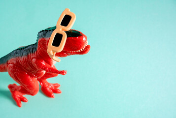 Fototapeta premium Coo red dinosaur wearing orange sunglasses on blue background. Copy space. Minimal art.