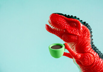 Close up red toy dinosaur holding cup of coffee on blue background.