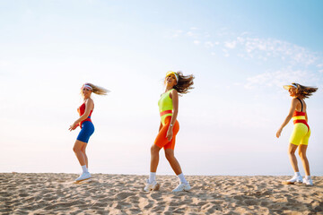 Happy woman in colorful swimsuits are dancing in the morning at the beach. Сoncept of sports, fitness, aerobics. Active sport.