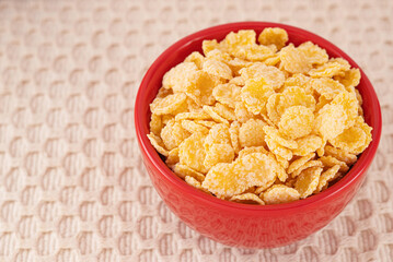 Red ceramic bowl of dry uncooked corn flakes. Traditional breakfast yellow cereal in isolated porcelain plate. 