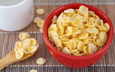 Red ceramic bowl of dry uncooked corn flakes. Traditional breakfast yellow cereal in isolated porcelain plate. 
