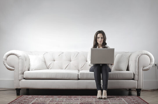 woman works with her computer sitting on a sofa