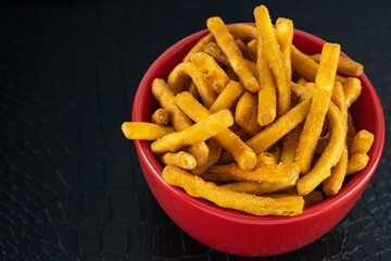 Wheat snack in the shape of cheese flavored sticks, cheese sticks in a red ceramic bowl on a black table. Bowl of Extra Thin Salted Stick Pretzels