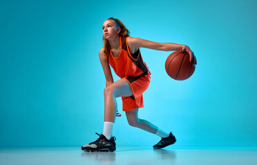 Young athletic girl, basketball player in motion, running with ball against blue studio background in neon light. Concept of professional sport, action and motion, game, competition, hobby, ad © master1305