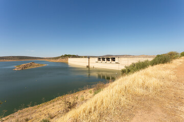 Fototapeta na wymiar General view of the swamp dam in the area where it contains water. Hydroelectric power station. The water level is high despite the drought. There is a small mound in the middle of the water. Spain. 