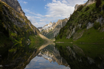 Fototapeta na wymiar Amazing mountain lake on a sunrise with super reflection and green shores in the Alps of Switzerland in the canton of Appenzell. The lake is called Fählensee.
