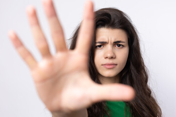 Fototapeta premium Portrait of a serious young woman showing stop gesture with her palm over white background