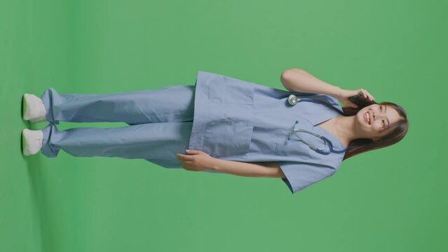 Full Body Of Asian Female Doctor With Stethoscope Talking On Smartphone While Standing On Green Screen Background In The Hospital
