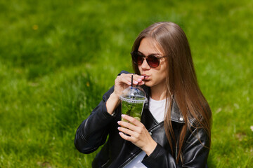young girl drinks a refreshing cocktail with ice on green grass