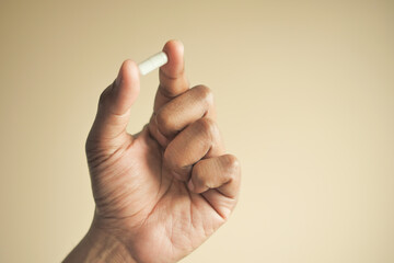 Close up of man hand holding capsule against orange background 