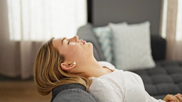 Young blonde woman relaxed on sofa with tired expression at home