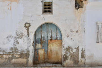 Fototapeta na wymiar Severely Weather-Beaten Exterior Wall and Door with Slight Keyhole Arch in Kairouan Old Town, Tunisia