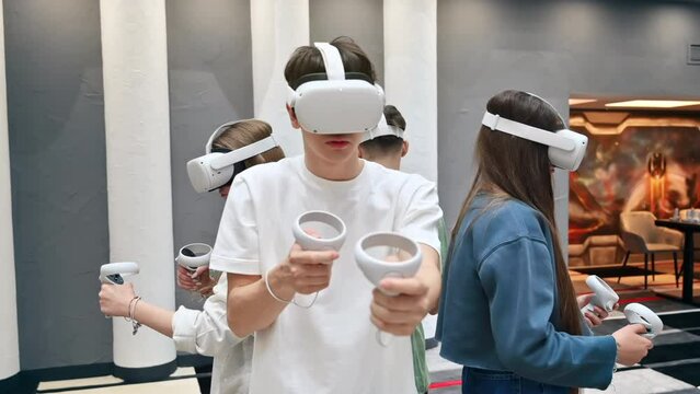 Group of four teens with VR headset and controllers playing games in a team on a VR arena. Slow motion