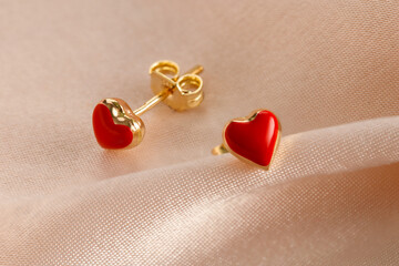 Hearts shape gold stud earrings  with red enamel on pink background. Romantic jewelry. Сoncept for Valentine's Day