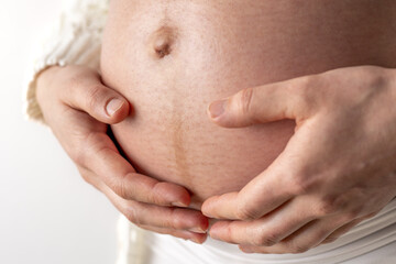 Pregnant woman gently holding her naked, round belly in final months of pregnancy. Third trimester...