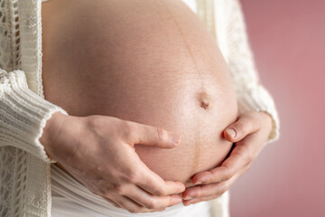 Pregnant woman gently holding her naked round belly in last month of pregnancy. Third trimester - week 36. Close up. Side view. Red background. Bright shot.