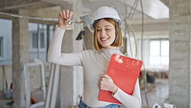 Young blonde woman architect holding keys of new home and clipboard at construction site
