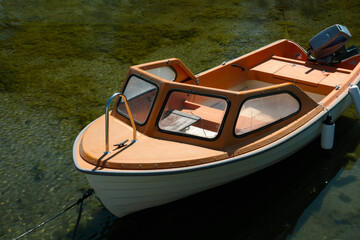 Obraz premium Small old orange motorboat moored in clear green water for summer recreation concept