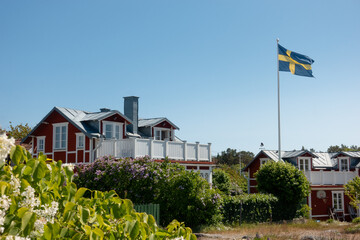 Traditional Swedish red house with white trims in residential area with flag of Sweden flying in summer picturesque scene